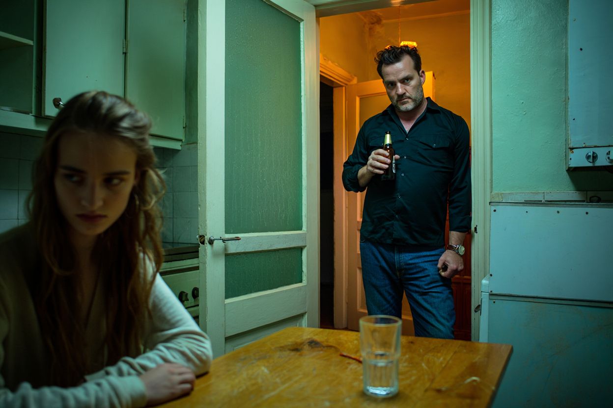 Девушка сидит за столом на фоне мужчины